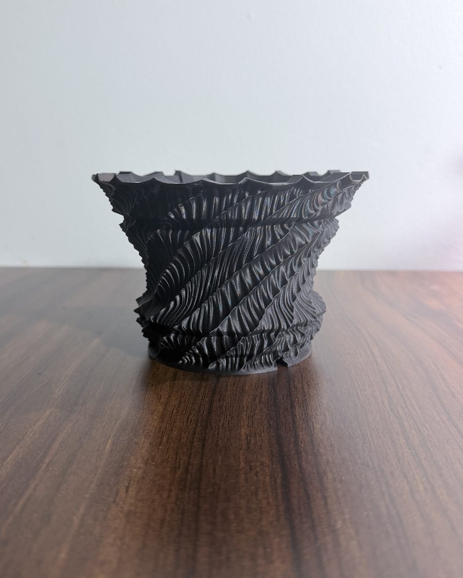 Black 3D-printed planter with ridges spiralling up the wall, on a wooden table